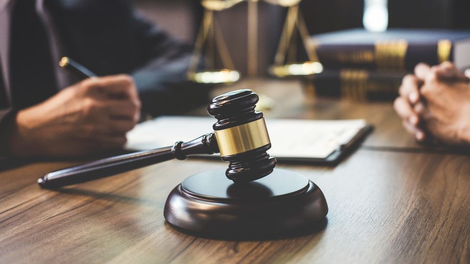 black gavel in the foreground, two people at a desk in the background